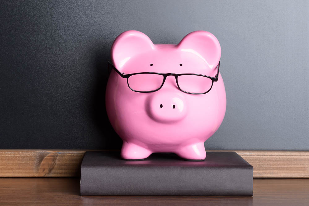 Pink Piggy Bank With Eye Glasses On Book Near Blackboard
